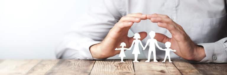 Hands forming a protective gesture over a paper-cutout family, symbolizing security and care.