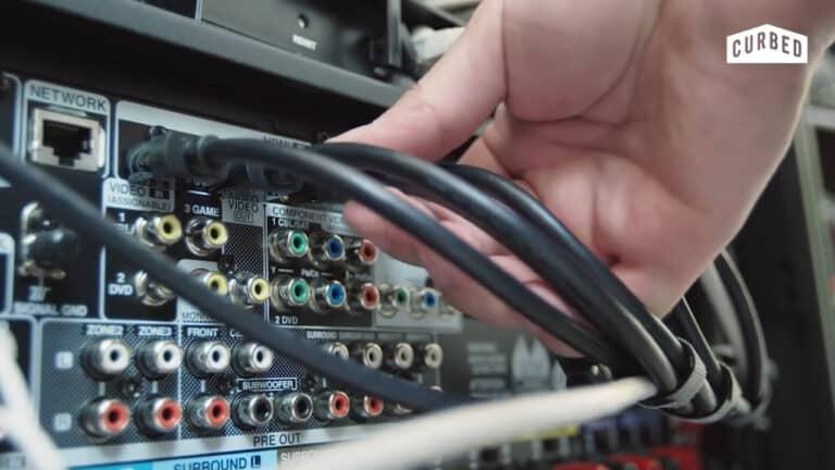 A person connecting cables to the back of an audio-video receiver with multiple input and output ports.