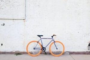 Bicycle with orange tires leaning against a white brick wall.