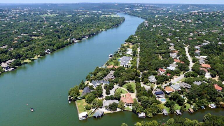 An aerial view of a scenic river surrounded by lush greenery and luxurious homes with private docks.