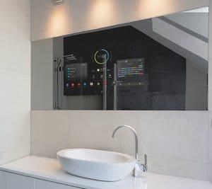 Modern smart mirror installed above a bathroom sink, displaying digital controls and information on the surface.