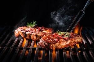 Juicy steaks cooking on a flaming grill with herbs and smoke rising, representing outdoor smart grilling technology.