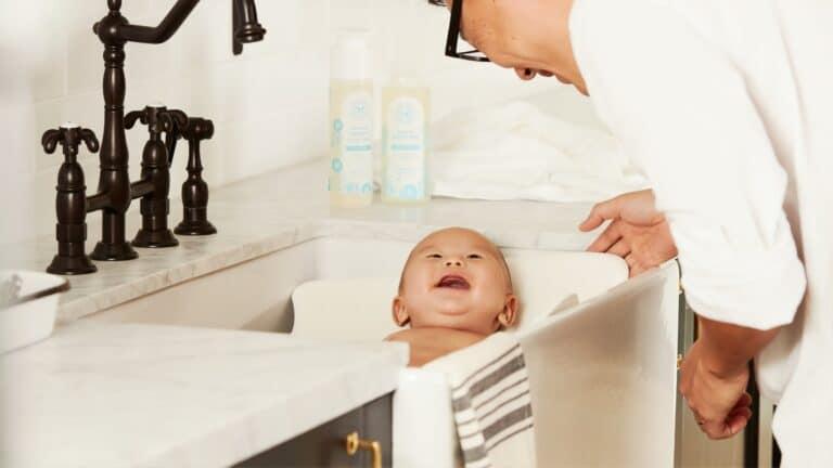 Infant enjoying bath time in a clean, modern sink with a caring adult, showcasing smart home technology in a bathroom.