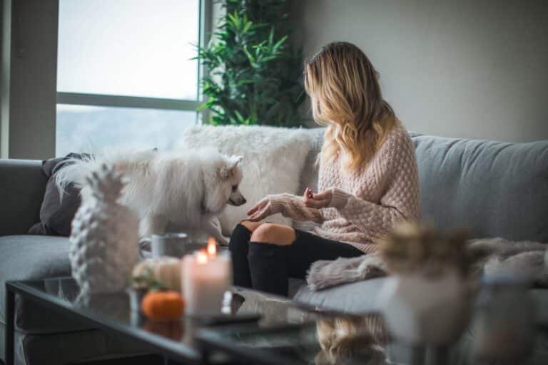 Woman sitting on a cozy couch with her dog in a warmly lit living room, representing winter home comfort and readiness