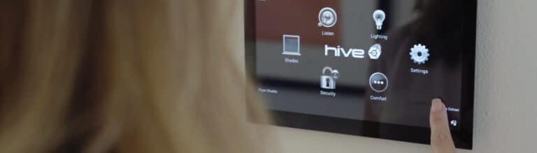 A person interacting with a wall-mounted smart home control panel displaying the Hive interface.
