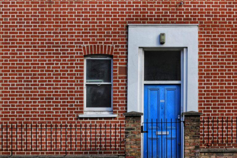 Bright blue door and single window on a red brick building.