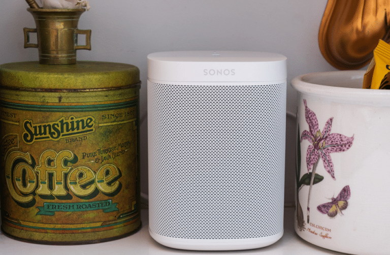 White Sonos speaker placed between a vintage coffee tin and a floral ceramic container.