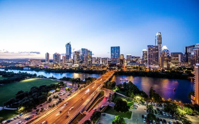 A stunning aerial view of a city skyline at dusk with a bridge, river, and illuminated buildings.