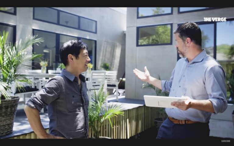 Two men discussing technology outdoors, one holding a tablet, representing troubleshooting with a smart home manager for better Wi-Fi coverage.