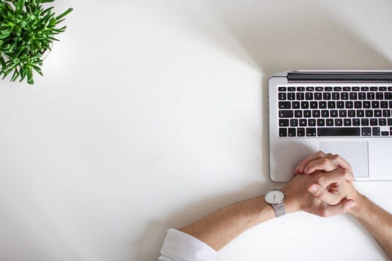 Hands clasped on a desk beside a laptop, symbolizing focus on home technology solutions and improving internet connectivity.