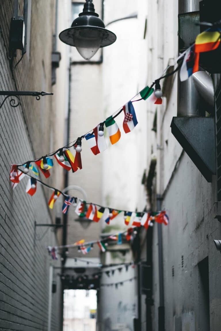 A narrow alleyway decorated with strings of international flags hanging under a vintage-style lamp.