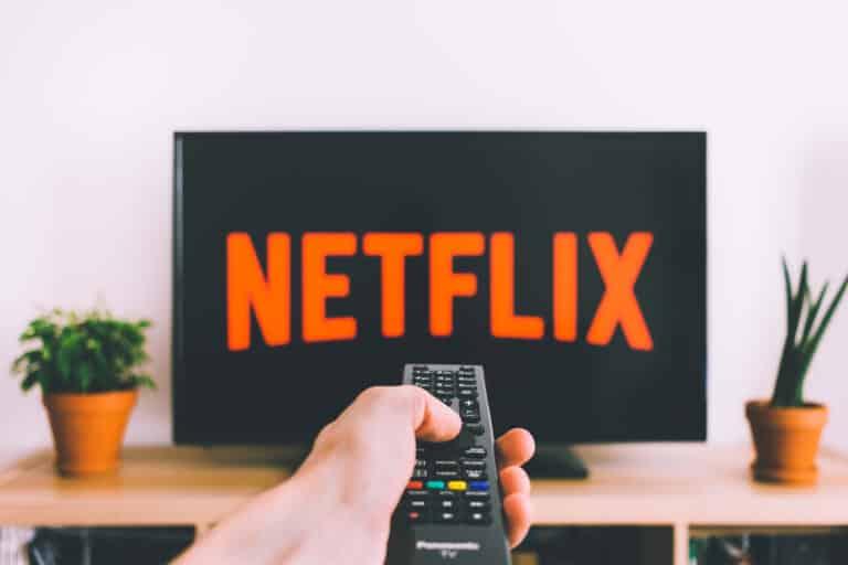 Hand holding a remote control pointed at a TV displaying the Netflix logo.