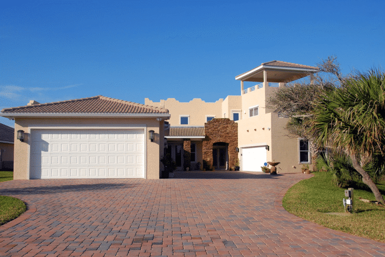 Modern residential home with a two-car garage, featuring a stone accent facade, landscaped front yard, and clear blue sky, highlighting smart home design elements.
