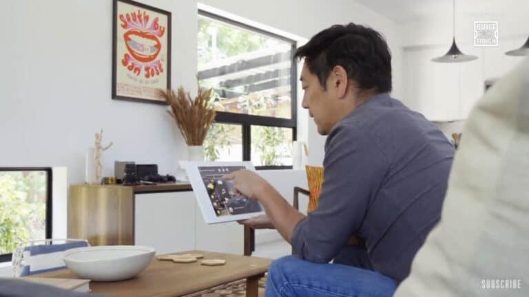Man using a tablet to control smart home devices in a modern living room, emphasizing home technology for comfort and security during quarantine.