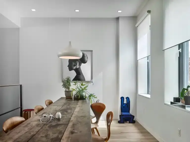 Modern dining area featuring a wooden table, stylish chairs, indoor plants, and Lutron shades, highlighting smart home design and automation aesthetics.