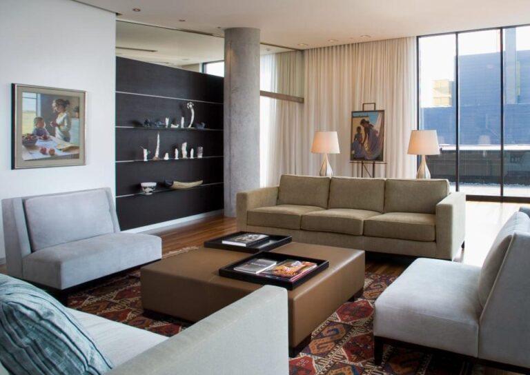 Modern living room with energy-efficient design, featuring a cozy sofa, stylish armchairs, decorative shelving, and large windows for natural light.