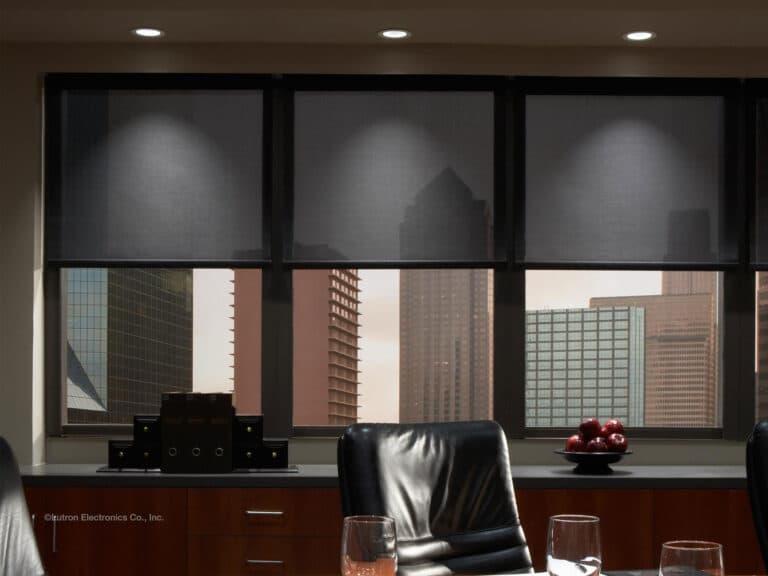 Motorized window shades partially lowered in a modern office with a city view through large windows.