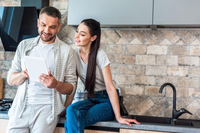Couple using a tablet in a modern kitchen, discussing smart home technology and innovations.