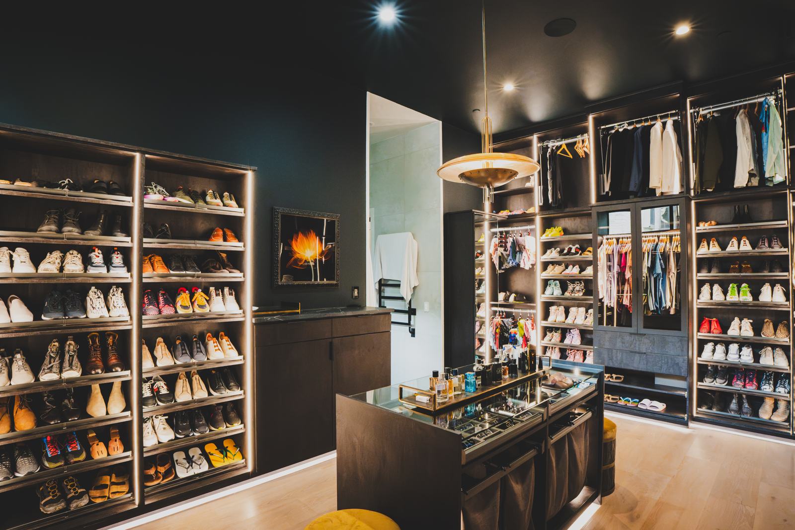 Walk-in closet with lit shoe shelves, a center island and a pendant light