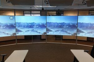 A curved multi-screen display showing a panoramic mountain landscape in a modern workspace.