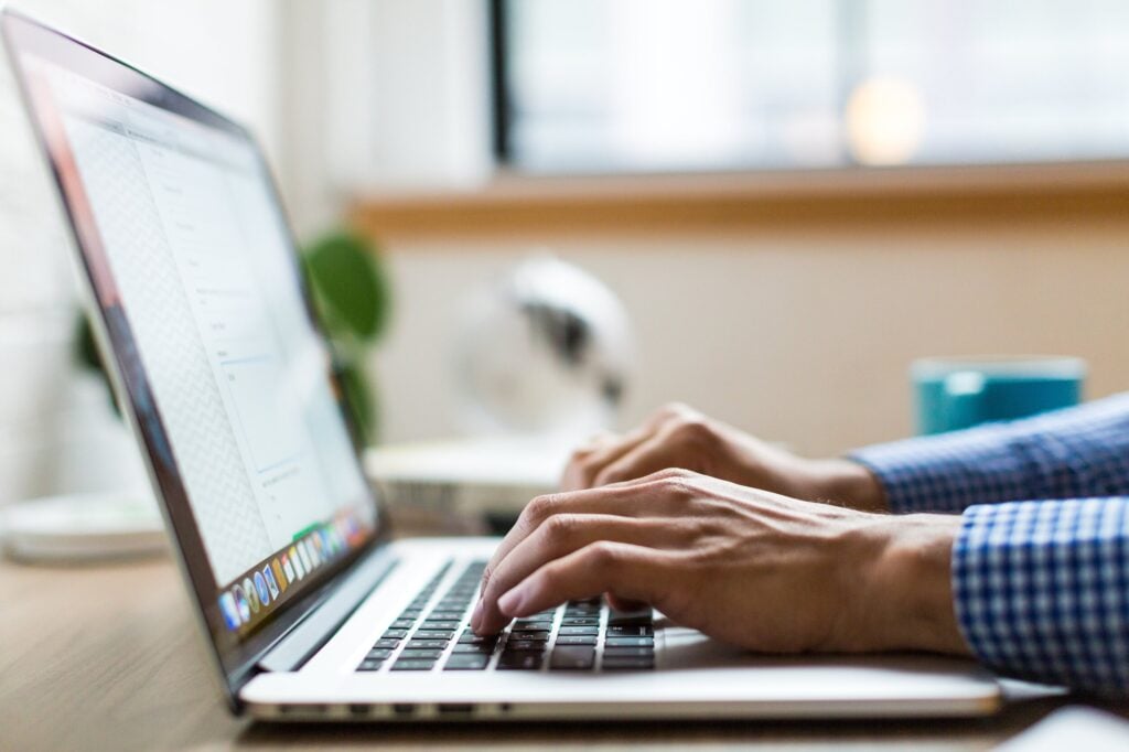 Hands typing on a laptop at a desk in a well-lit room.