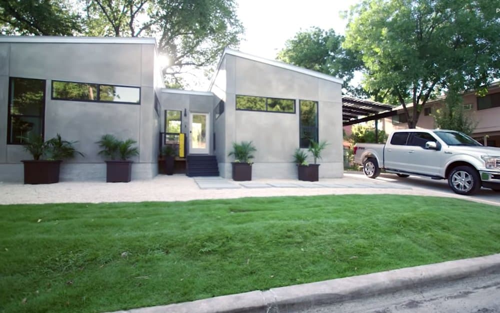 A modern home with large windows, a landscaped yard, and a silver pickup truck parked in the driveway.