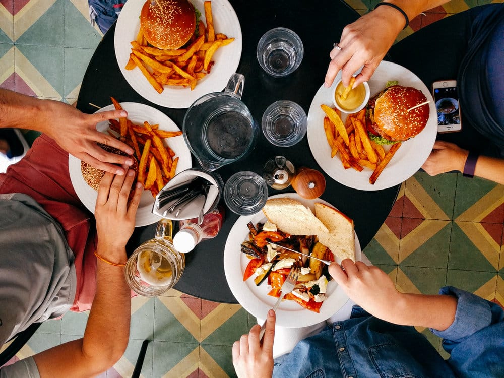 A top-down view of a group enjoying burgers, fries, and a sandwich at a restaurant table.