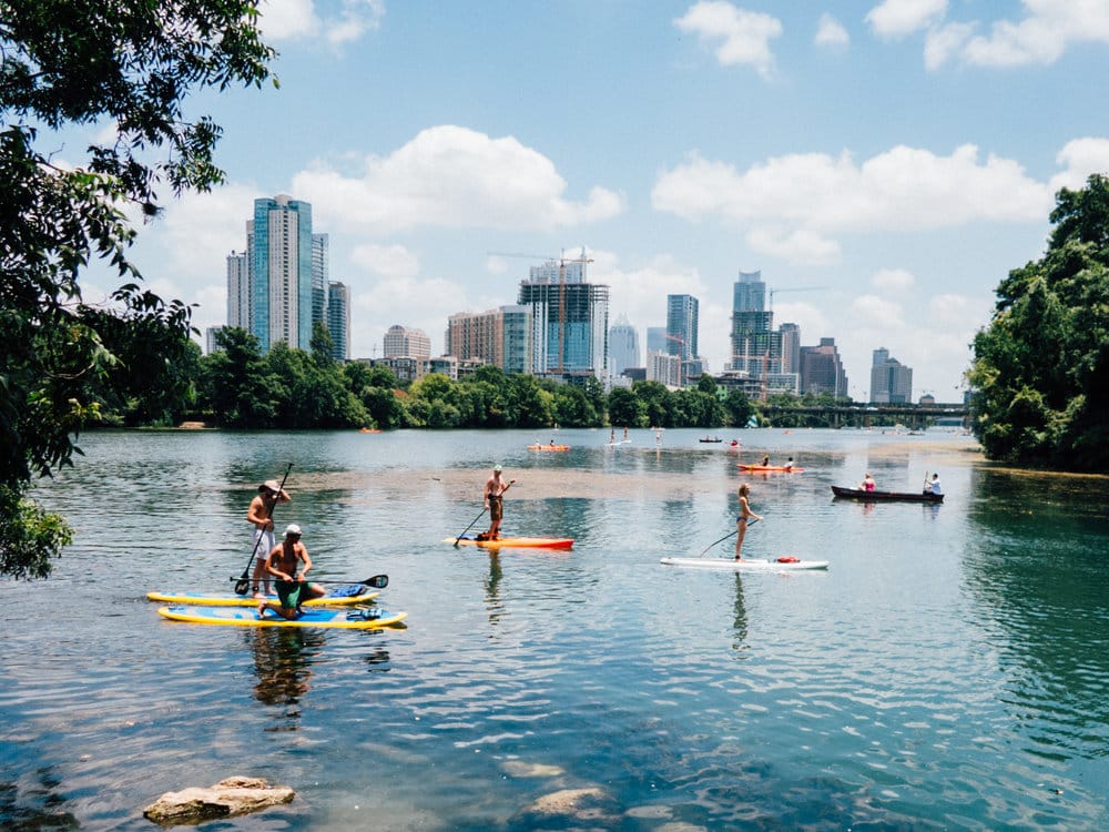 People paddleboarding and kayaking on a river with a city skyline in the background.