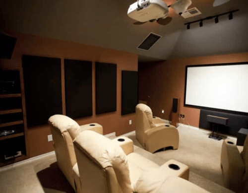 Home theater room with beige recliner seating, acoustic panels on the walls, a ceiling-mounted projector, and a large projection screen.