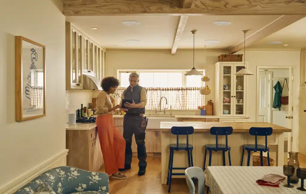 A technician and a homeowner discuss something on a tablet in a cozy, well-lit kitchen.
