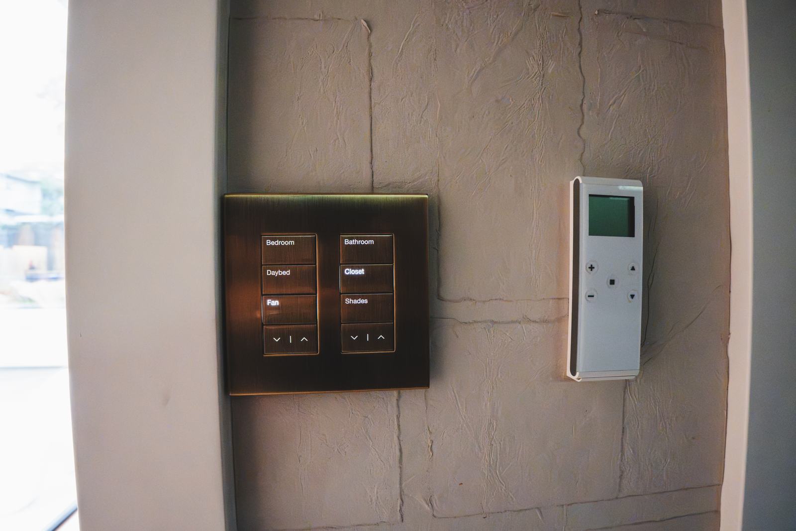 Two engraved Lutron Palladiom keypads in a bronze finish on a textured wall, beside a thermostat