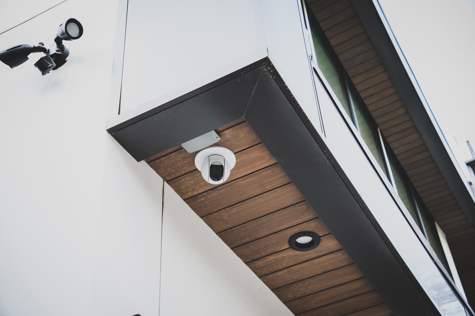 Security camera and floodlight mounted under a wood eave