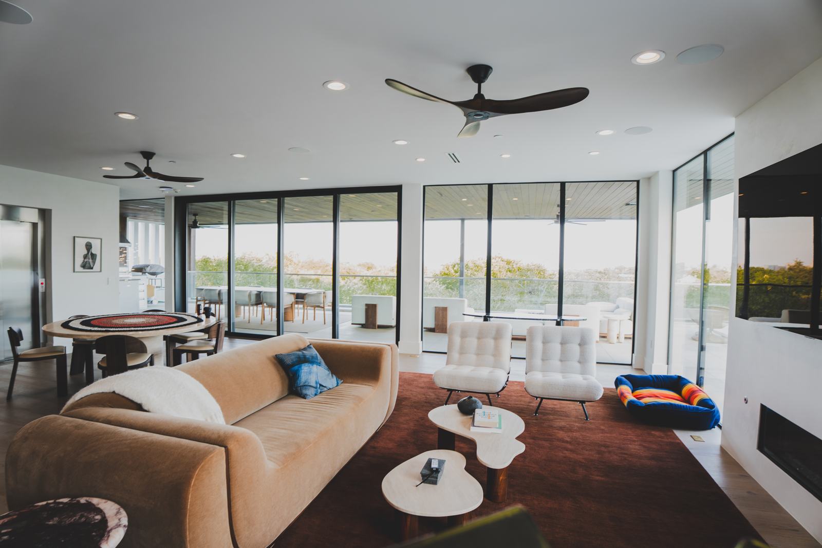 Upper-floor entertainment room with sofas, a game table, ceiling fans and a wall of windows